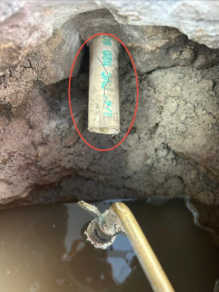 Split running down a three quarter inch PVC spa air line pipe exposed in a muddy excavation and circled in red