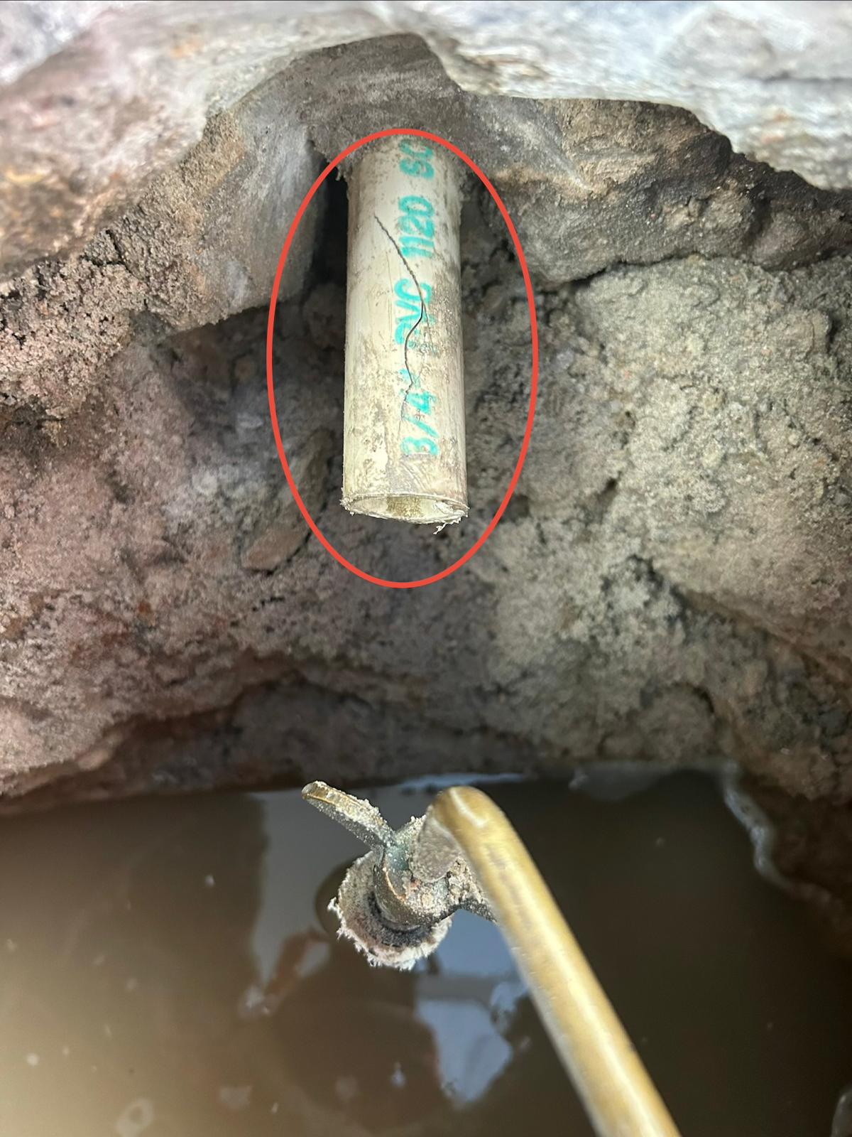 Split running down a three quarter inch PVC spa air line pipe exposed in a muddy excavation and circled in red
