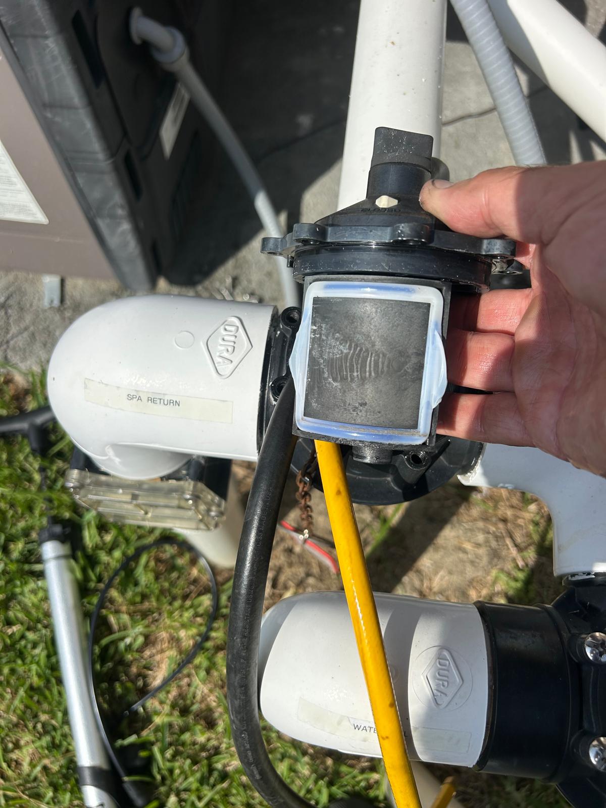 Worn diverter plate and deteriorated seal lifted out of a pool valve at an equipment pad with spa return and waterfall lines labeled