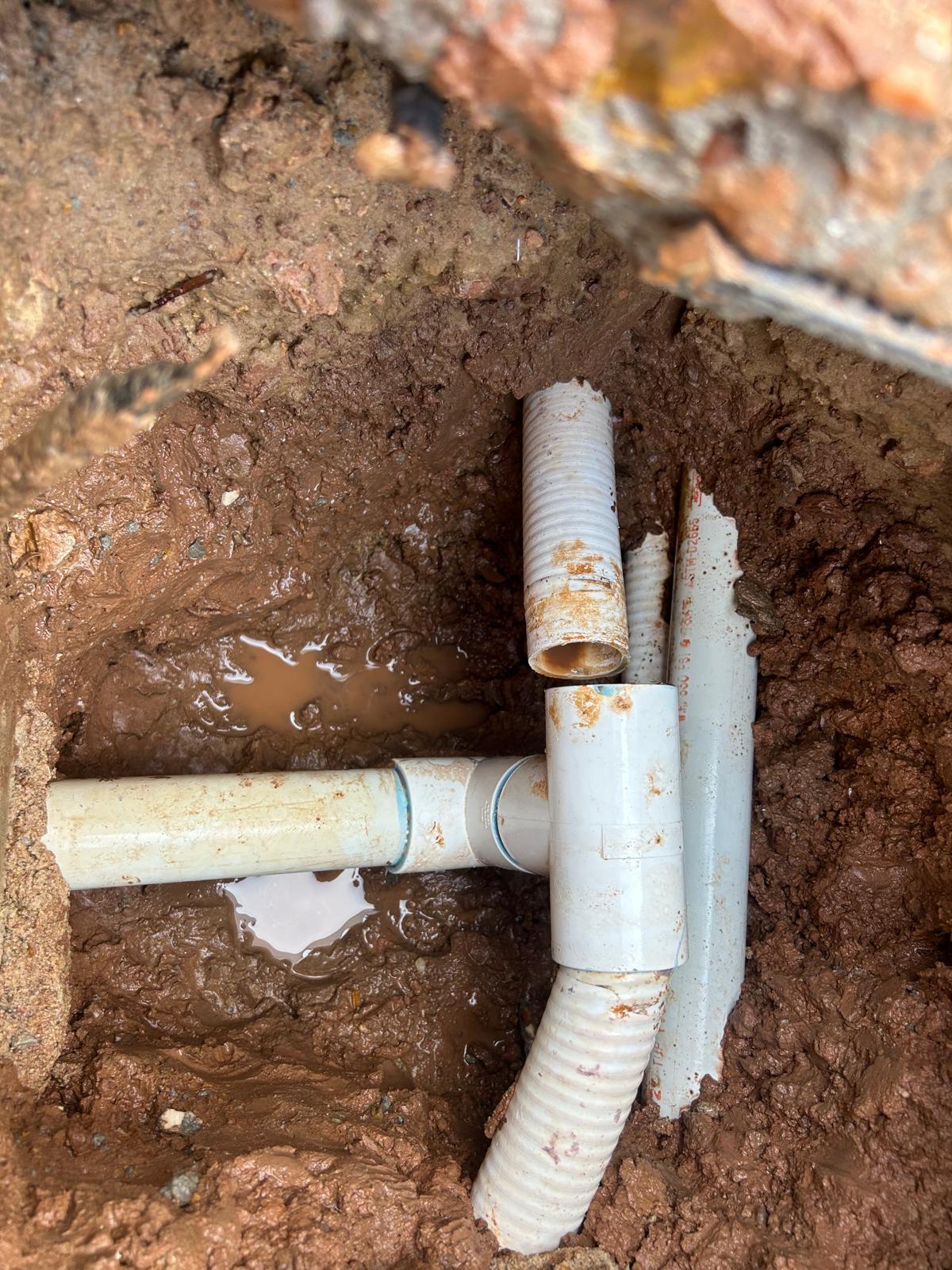 Corrugated flexible pool pipe glued into a PVC tee sitting in wet Houston clay, rust stained around the joint