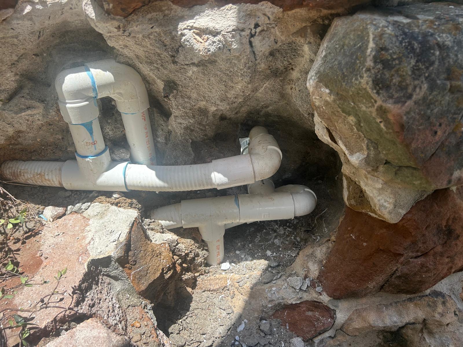 Freshly built PVC manifold with hand labeled lines tucked behind boulder coping during a pool water feature replumb