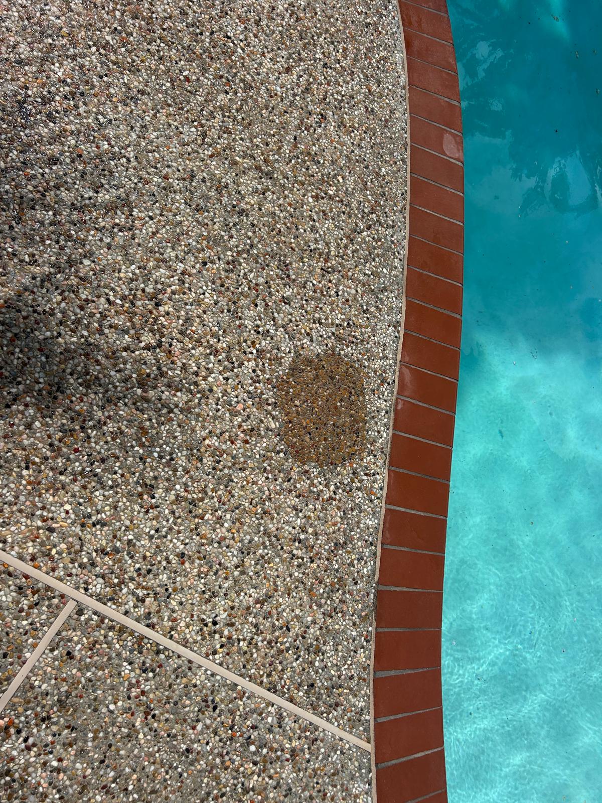 Exposed aggregate pool deck patched with matching pea gravel after an underground return line repair, beside red brick coping