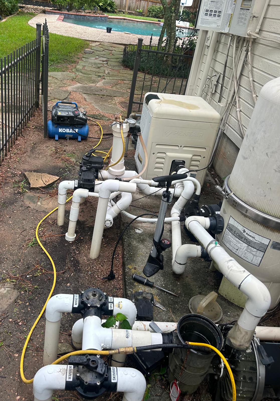 Air compressor and pressure gauge connected to labeled skimmer, main drain and spa valves at a Houston pool equipment pad during leak detection
