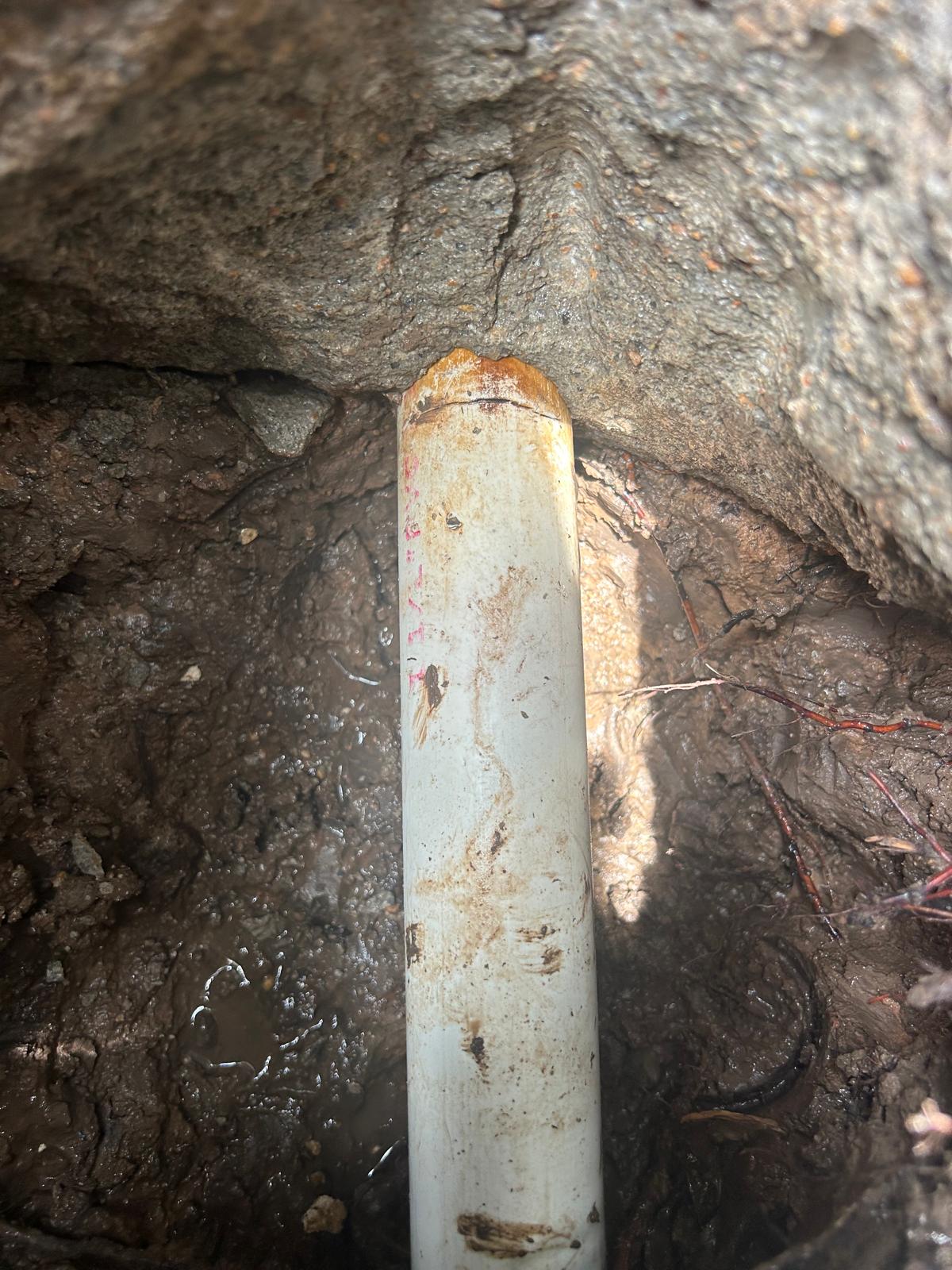 Excavated pool line with a crack across the top of the pipe at the point where it passes under the edge of the concrete deck