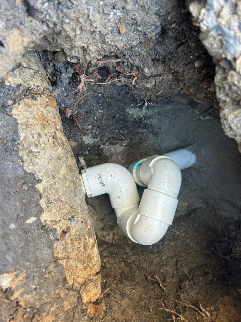 New PVC elbows spliced into a pool return line inside a compact excavation at the edge of the pool shell
