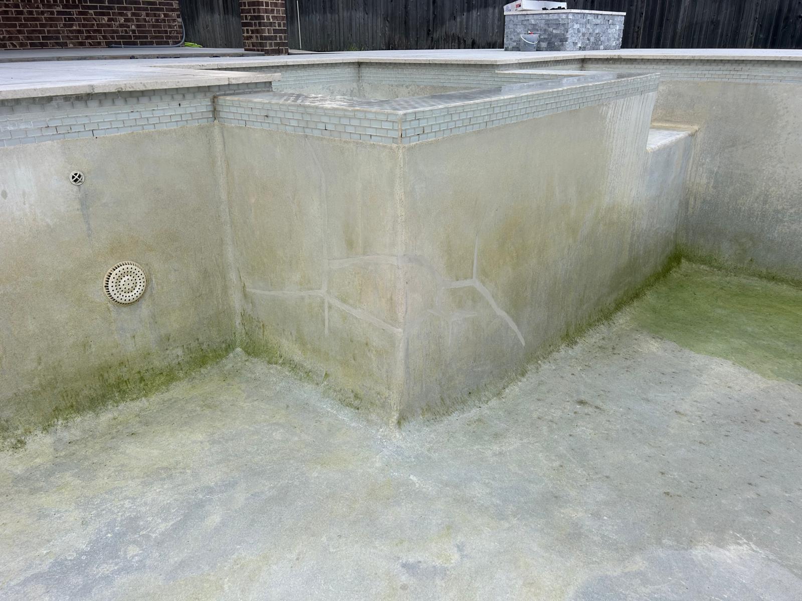 The same drained pool wall after its structural cracks were filled, with the repaired lines visible against the old surface