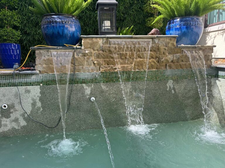 Four sheer descent water features running off a stone wall into a pool with green mosaic waterline tile