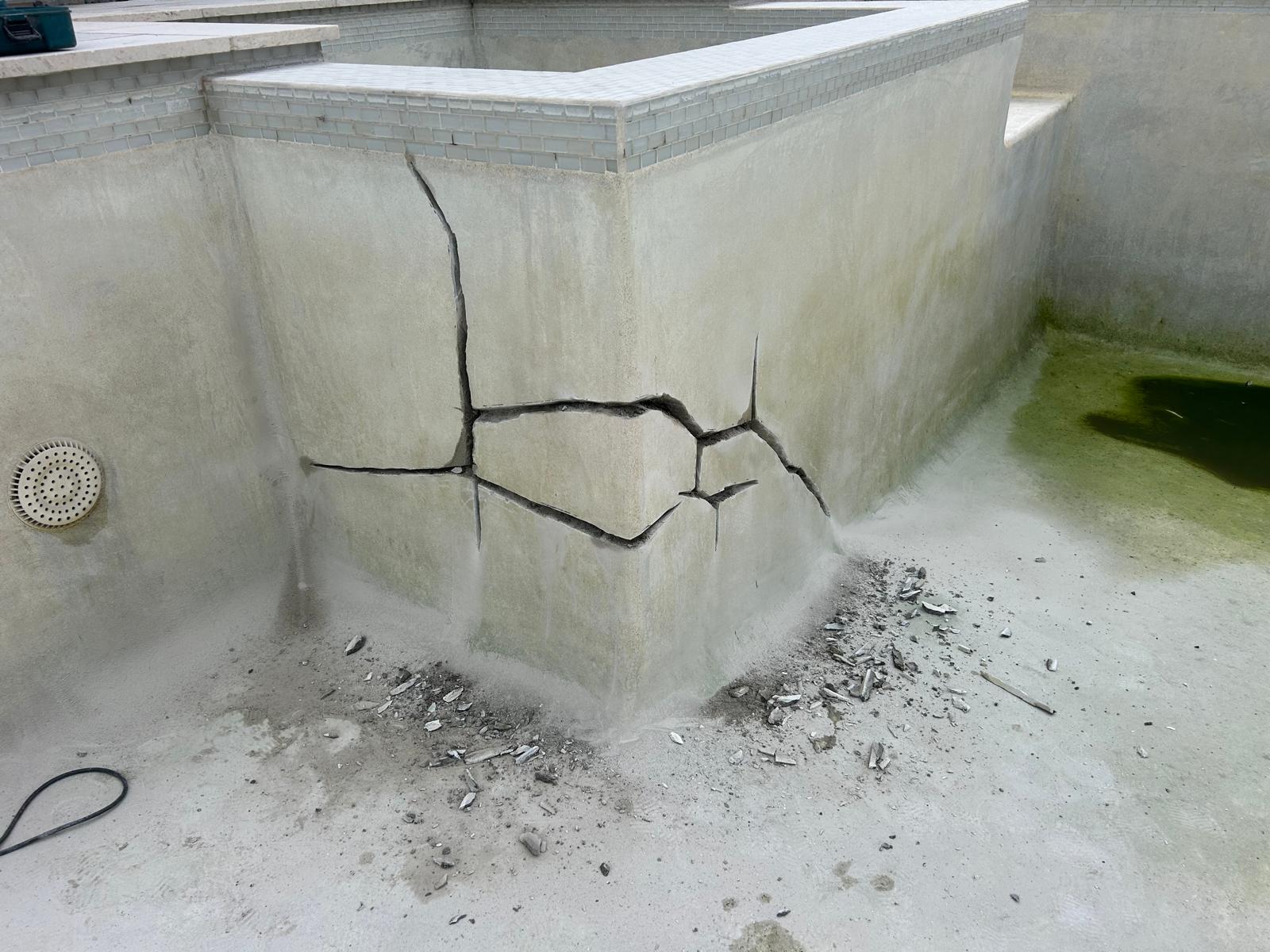 Structural cracks routed out along the raised wall of a drained gunite pool with plaster chips on the pool floor