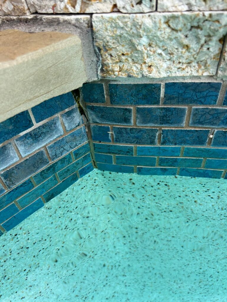 Vertical crack running down the tiled inside corner of a spa with algae growth along the crack line