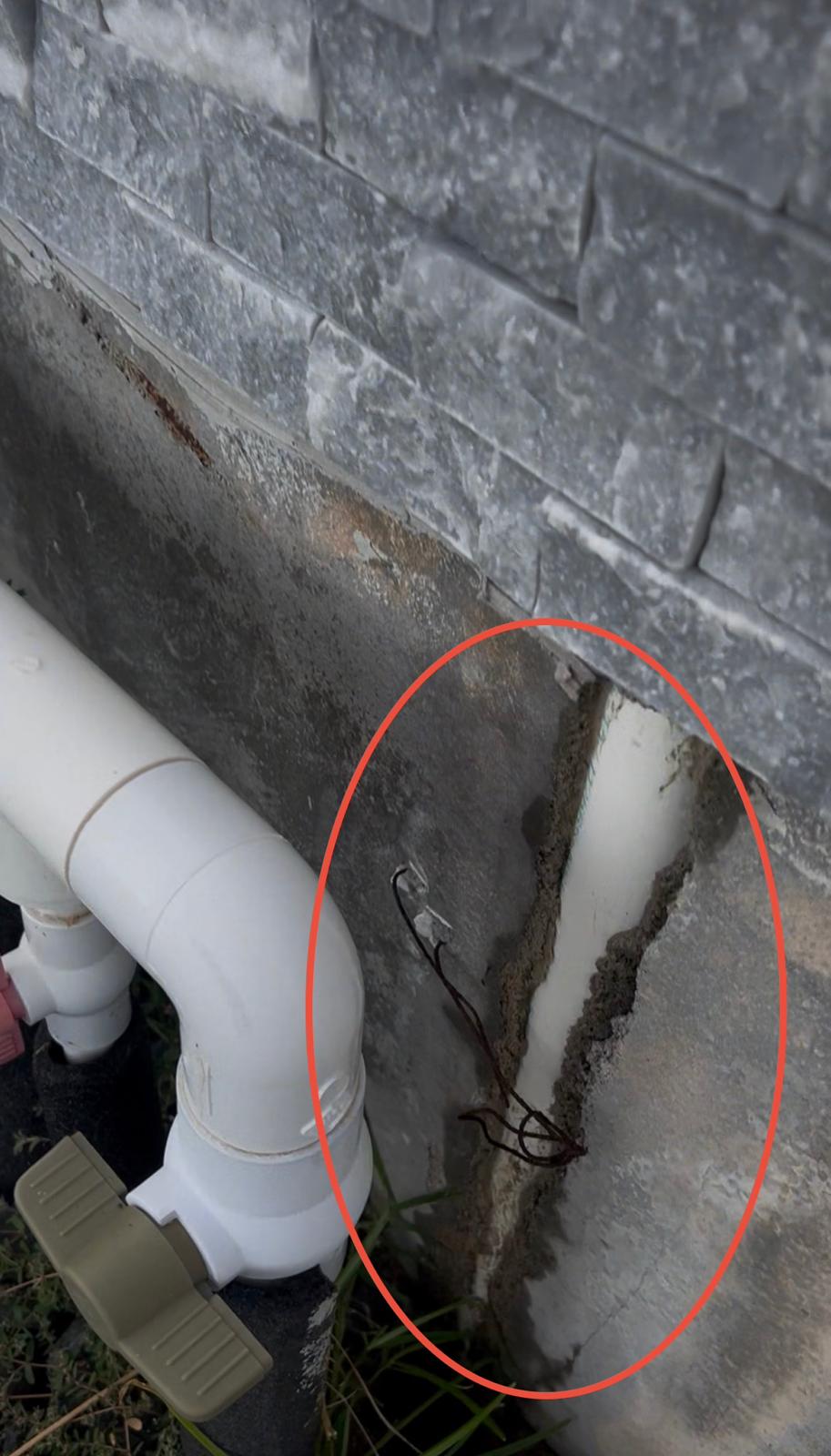 PVC water feature supply pipe uncovered inside a stacked stone wall with rust staining and efflorescence around the opening