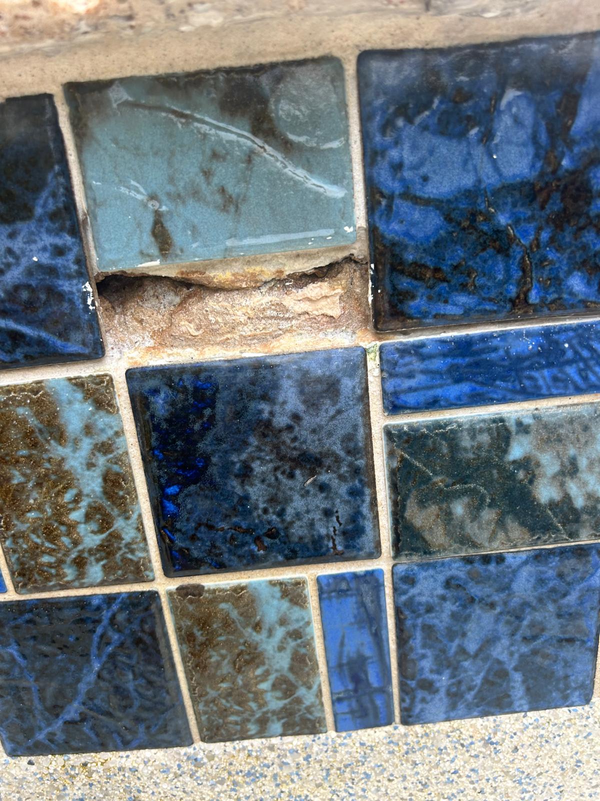 One waterline tile missing from a blue mosaic band with rust and mineral staining on the substrate behind it